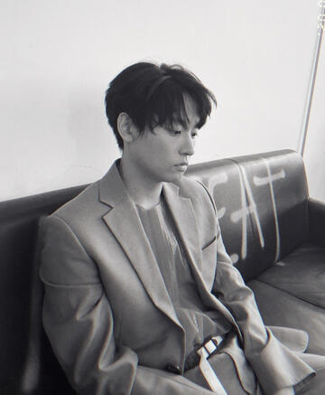 monochrome photo of inseong of sf9, wearing a casual blazer over a t-shirt, sitting on a leather couch looking melancholy